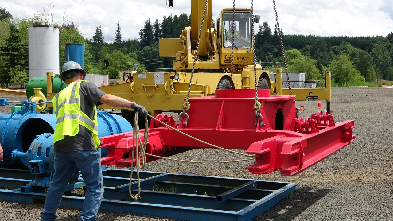 A worker in high-visibility clothing secures a large red load with chains to a Grove mobile crane during a safety training program at an ITI training center.